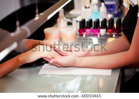 The manicurist holds hands of the client in beauty salon on desktop for manicure with nail polishes, napkins, creams and lighting instruments