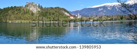 Crystal clear waters and snow-capped mountains at Lake Bled, Slovenia: Wide panorama of Lake Bled in the spring featuring Bled Castle and snowy mountain peaks reflecting in the clear waters