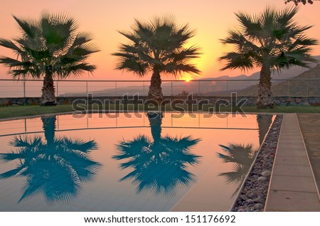 Aegean Sunrise - Summer sunrise over the Cretan mountains with palm trees reflecting in a pool in Malia, Crete