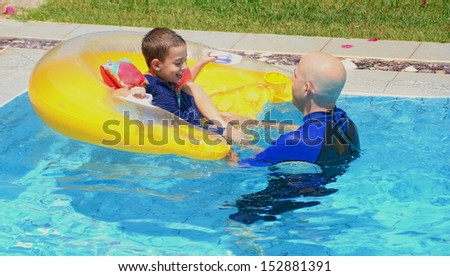 Father and son in a swimming pool - father and son having fun in the swimming pool with a floating cushion / seat