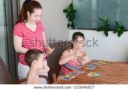 Family card game - teenage sisters and their younger brother playing a game of cards