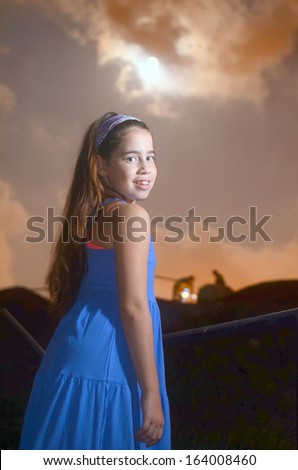A girl in a blue dress at night with a cloudy moon