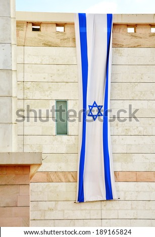 Israel flag in white and blue showing the Star of David hanging vertically on a modern building for Israel\'s Independence Day (Yom Haatzmaut)