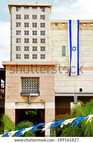 Israel flag in white and blue showing the Star of David hanging vertically on a modern building for Israel\'s Independence Day (Yom Haatzmaut)