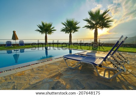 Palm trees, lounge chairs, and pool on a summer vacation - Sunrise and mist over the Cretan mountains with picture-perfect palm trees reflecting in a pool in Malia, Crete near Heraklion (HDR image)