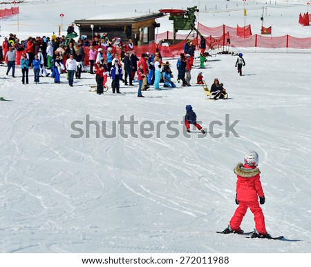 ZURS, AUSTRIA - APRIL 10, 2015: Kids skiing in a the Zurs - Lech, Arlberg, ski school. Parents and spectators are watching the kids racing on the final school day.  Conveyor is used to go up the hill.