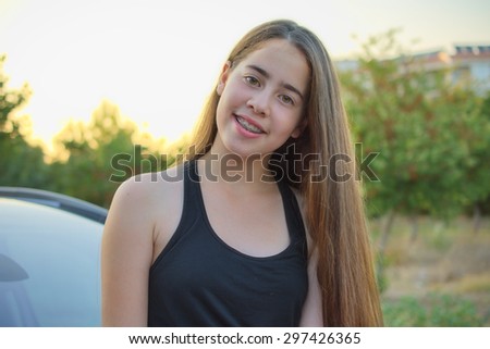 A 13 year old teenage girl with braces on her teeth sitting on a car  enjoying the Israeli summer sunset
