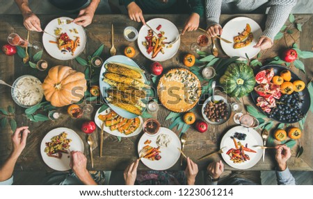 Vegan or vegetarian Thanksgiving, Friendsgiving holiday celebration. Flat-lay of friends eating meals at Thanksgiving Day table with pumpkin pie, roasted vegetables, fruit, rose wine, top view