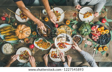 Traditional Thanksgiving or Friendsgiving holiday celebration party. Flat-lay of friends feasting at Thanksgiving Day table with turkey, pumpkin pie, roasted seasonal vegetables and fruit, top view