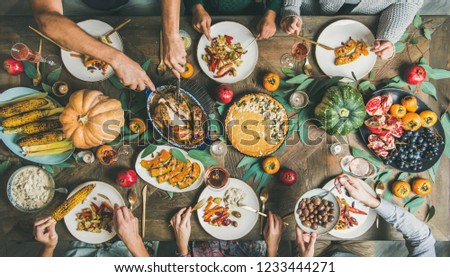 Thanksgiving or Friendsgiving holiday celebration party. Flat-lay of friends feasting at Thanksgiving Day table with turkey, pumpkin pie, roasted vegetables, fruit and rose wine, top view