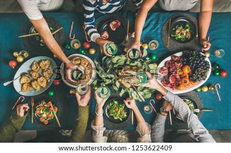 Company of friends gathering for Christmas or New Year party dinner at festive table. Flat-lay of human hands holding glasses with drinks, feasting and celebrating holiday together, top view