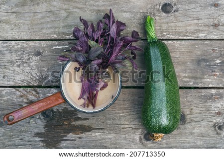 A marrow and a bunch of basil in an old metal scoop on a wooden table