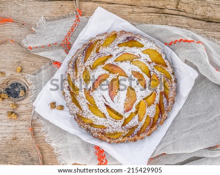 Peach pie with sugar powder over a piece of paper and a linen table cloth on a rough old wooden surface