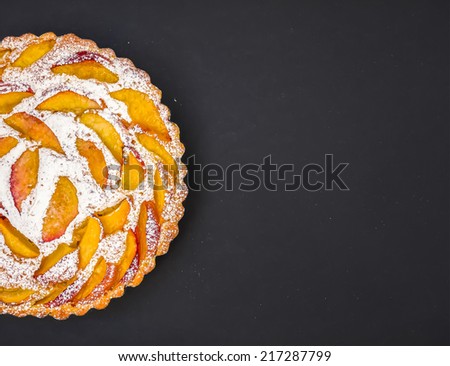 Peach pie with sugar powder over a dark surface with a space for your words