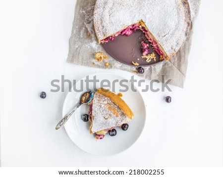 Custard cherry pie with fresh cherries and piece of pie on saucer with a spoon on a white background