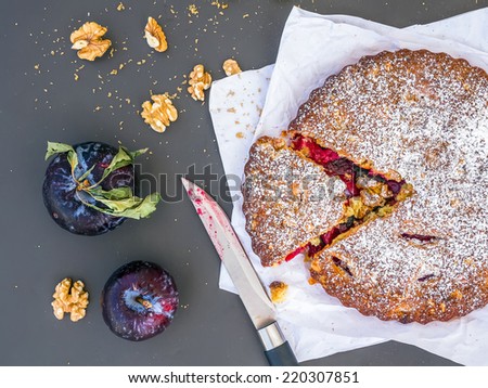 Plum cake with walnuts and fresh ripe plums on white paper over a black background