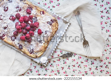 Raspberry cottage cheese cake with fresh raspberries, almond petals and sugar powder on a silver tray over a flower pattern table cloth