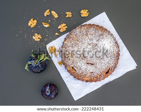 Plum cake with walnuts and fresh ripe plums on white paper over a black background