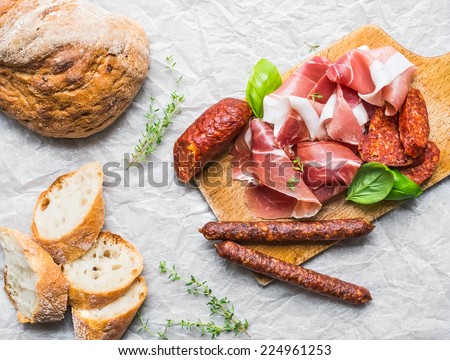 Meat appetizers selection, a loaf of rustic village bread and baguette slices on a white paper background