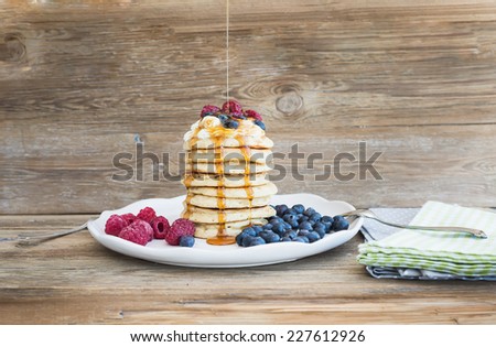 Pancakes with creamy cheese topping, garden berries and maple syrup over a rustic wooden background