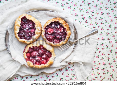 Small rustic berry galettes on silver dish over a floral patterned table cloth