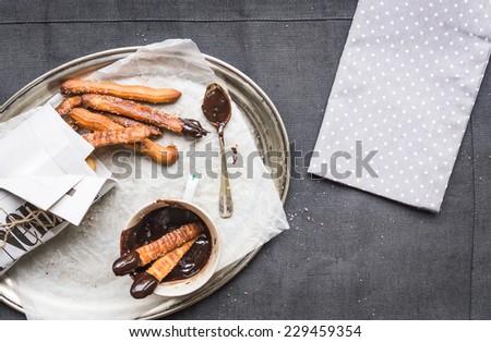 Churros with chocolate sauce on a metal plate over a linen table cloth