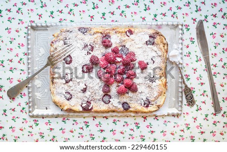 Raspberry cottage cheese cake with fresh raspberries, almond petals and sugar powder on a silver tray over a flower pattern table cloth