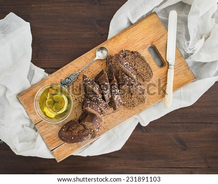 Dark baguette cut in slices with olive oil on a rustic wooden board over a dark wood background