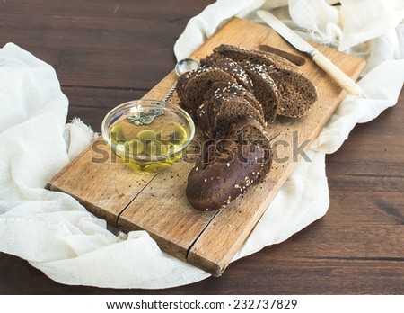 Dark baguette cut in slices with olive oil on a rustic wooden board over a piece of white linen fabric and dark wood background (selective focus)