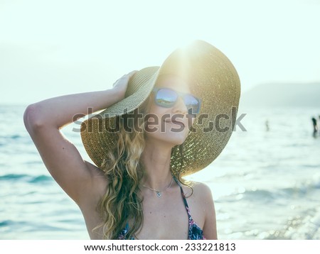 Young blondy girl in sunglasses and straw hat at the beach enjoying the sun