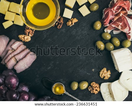 Wine appetizer set: cheese and meat selection with grapes, honey, olives and walnuts on black stone background with a copy space in the center. Top view