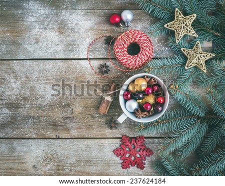 Christmas (New Year) decoration background: a cup full of colorful Christmas tree toys, cinnamon sticks, glittering toy stars and a decoration rope on a rustic wood background. Top view