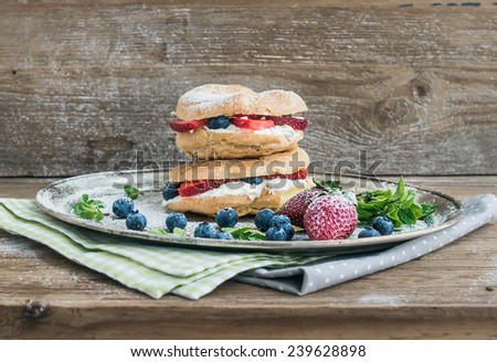Custard ring pastry filled with cream-cheese, fresh strawberry and raspberry on a silver tray over a rough wood background