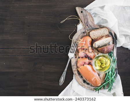 Appetizer set: chicken carpaccio, bread, olives, spices and rosemary on a rustic wooden board and a piece of linen fabric over a dark wood background with a copy space. Top view