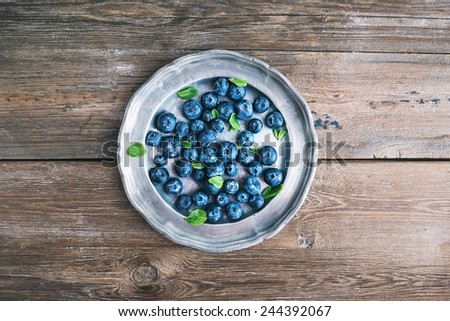 An old vintage metal plate full of fresh ripe blueberries over a rustic wooden desk background, top view