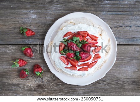 Rustic Pavlova cake with fresh strawberries and whipped cream over a rough wood background. Top view