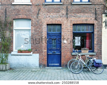 Bicycles parked at the entrance of the old medieval red brick house with violet door in a street in Bruges, Belgium, Western Europe