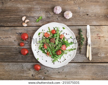 Salad with arugula, cherry tomatoes, sunflower seeds and herbs on white ceramic plate over rustic wood background, top view