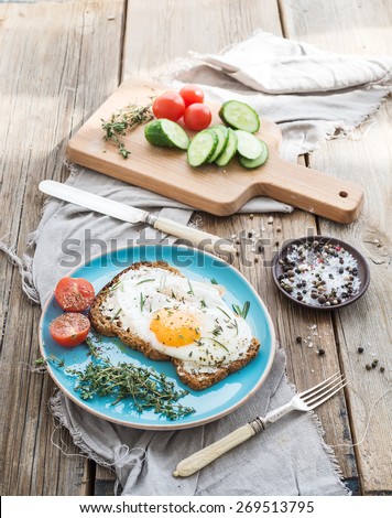 Breakfast set. Whole grain sandwich with fried egg, vegetables and herbs on rustic wooden table, morning mood, top view