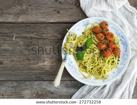 Pasta spaghetti with pesto sauce, basil, baked cherry-tomatoes on rustic wooden table , top view, copy space