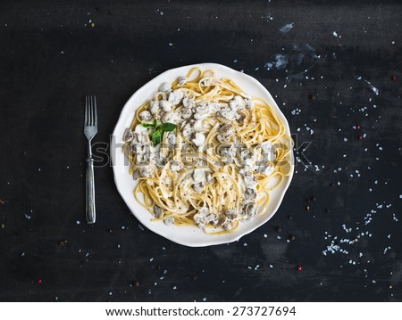 Pasta spaghetti with creamy mushroom sauce and basil in white ceramic plate over old grunge dark table, top view, copy space