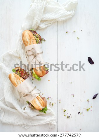 Sandwiches with beef, fresh vegetables and herbs over white wood backdrop, top view, copy space