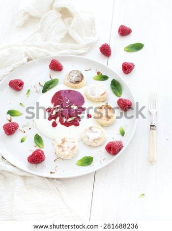 Rustic breakfast set. Russian cottage cheese cakes on a white ceramic plate with berry jam, almonds, fresh raspberries and mint over white wooden backdrop, top view, copy space