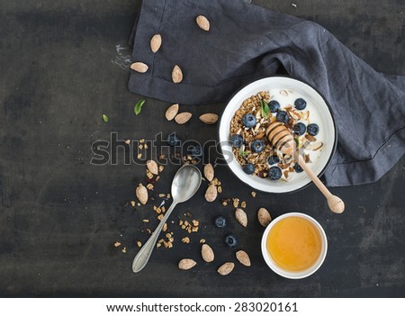 Healthy breakfast. Oat granola with fresh blueberries, almond, yogurt and mint in a rustic metal bowl over dark grunge surface. Top view, copy space