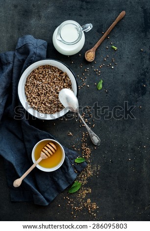 Rustic healthy breakfast set. Cooked buckwheat groats with milk and honey on dark grunge backdrop. Top view, copy space