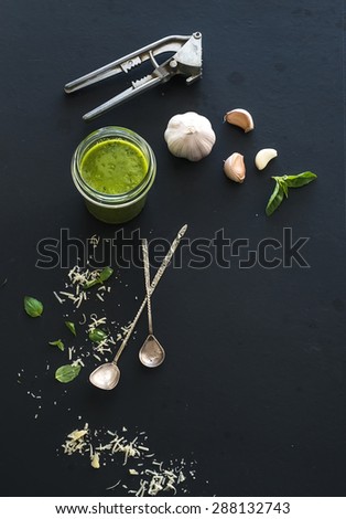 Jar of fresh home made pesto and ingredients for it. Fresh basil leaves, grated parmesan cheese and garlic over black backdrop. Top view, copy space