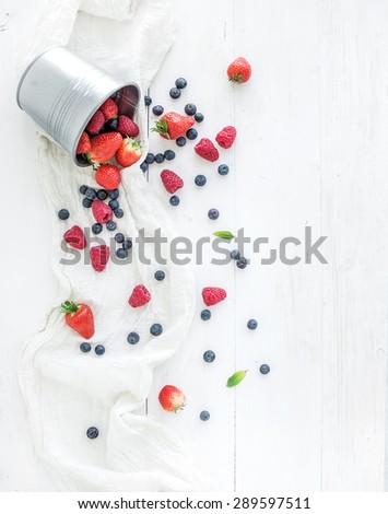 Berry frame with copy space on right. Metal bucket, strawberries, raspberries, blueberries and mint leaves, white wooden background, top view, copy space