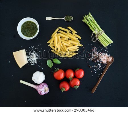 Ingredients for cooking pasta. Penne, green asparagus, basil, pesto sauce, garlic, spices, parmesan cheese and  cherry-tomatoes on dark grunge backdrop, top view