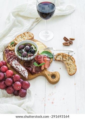 Wine appetizer set. Red wine, grapes, honey, parmesan cheese, meat variety, bread slices, pecan nuts, honey, olives and basil on rustic wooden board over white wood backdrop, top view, copy space