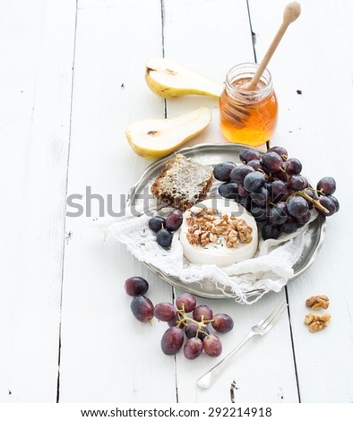 Camembert cheese with grape, walnuts, pear and honey on vintage metal plate over white rustic wood backdrop, copy space